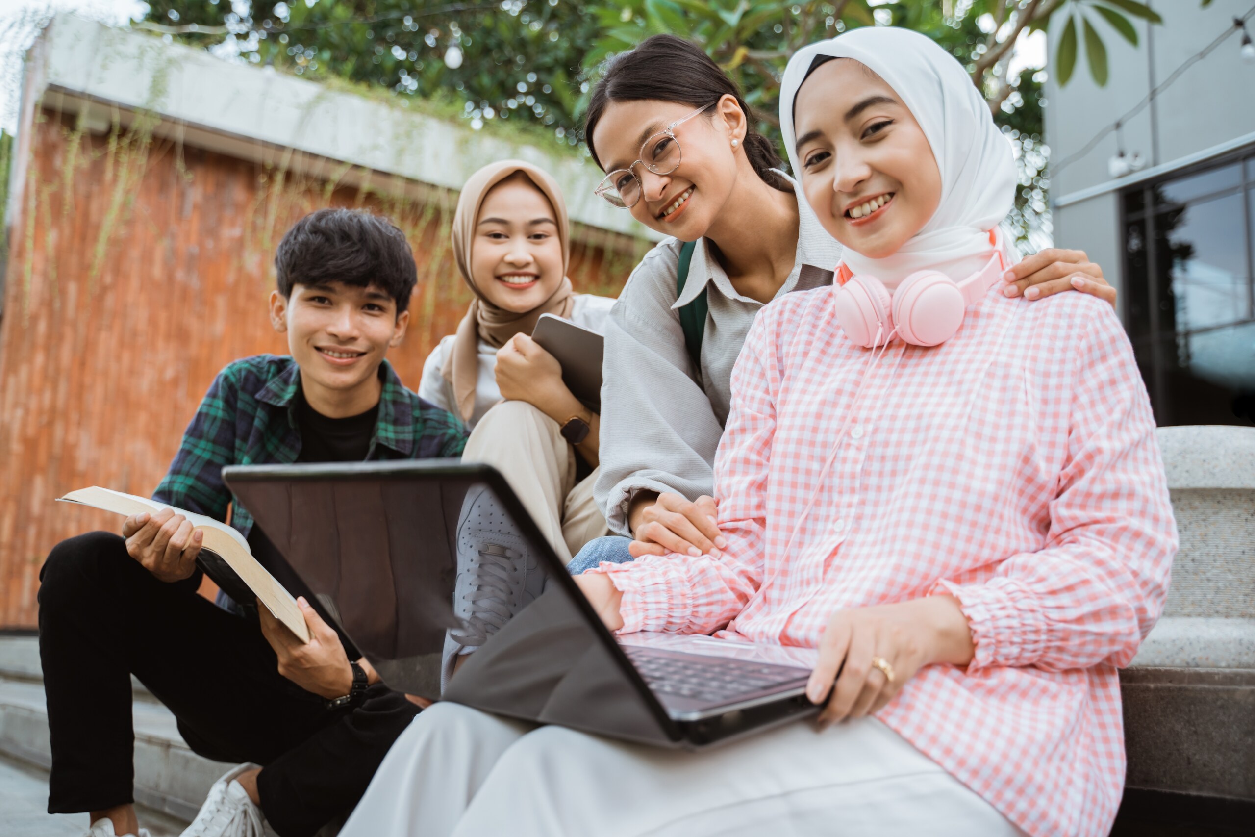 Four students sitting together outdoors with books and tablets