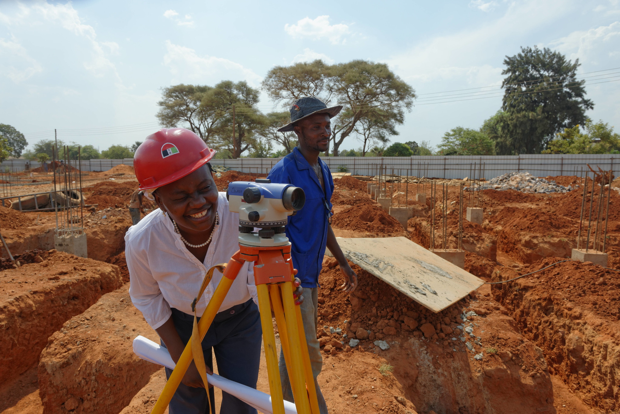 Construction workers using surveying equipment on a site in Zambia